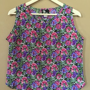 May include: A sleeveless floral print top with a scoop neck. The print features pink, purple, and green flowers on a black background. The tag on the top reads "Tella" in white text.