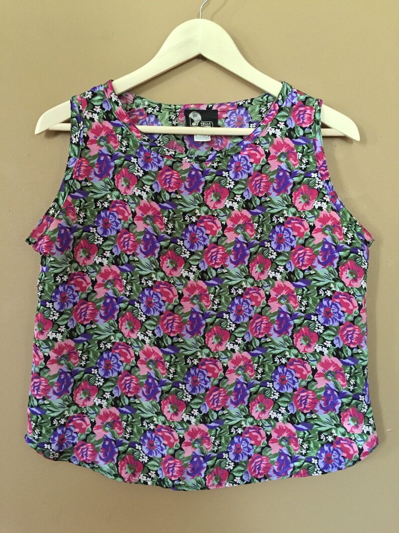 May include: A sleeveless floral print top with a scoop neck. The print features pink, purple, and green flowers on a black background. The tag on the top reads "Tella" in white text.