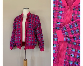 Puede incluir: Una vibrante chaqueta bomber rosa con un estampado de cuadros en tonos rosa, azul y negro. La chaqueta tiene una cremallera completa, puños de canalé y un cuello. La chaqueta se exhibe en un maniquí.