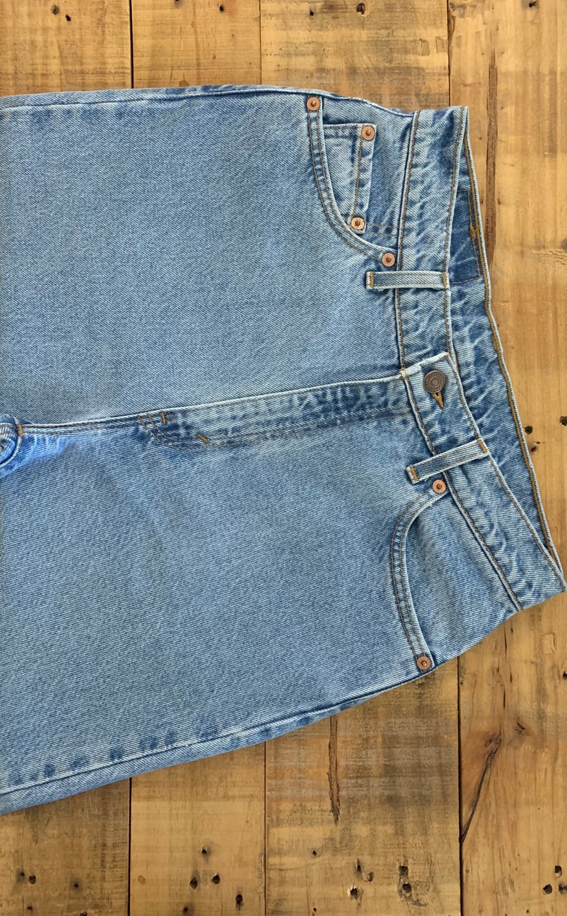 May include: Light blue denim jeans with classic five-pocket styling. The jeans feature copper rivets, a button closure, and a straight leg design. The garment is made of durable denim fabric.