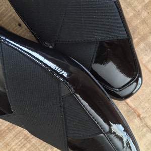 May include: A pair of black patent leather shoes with a criss-cross strap design. The straps are made of a black fabric.