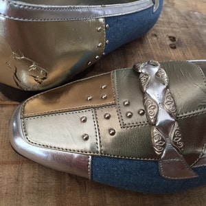 Puede incluir: Un par de zapatos de cuero plateado y dorado con detalles de denim. Los zapatos tienen un detalle de cadena plateada y tachuelas plateadas.