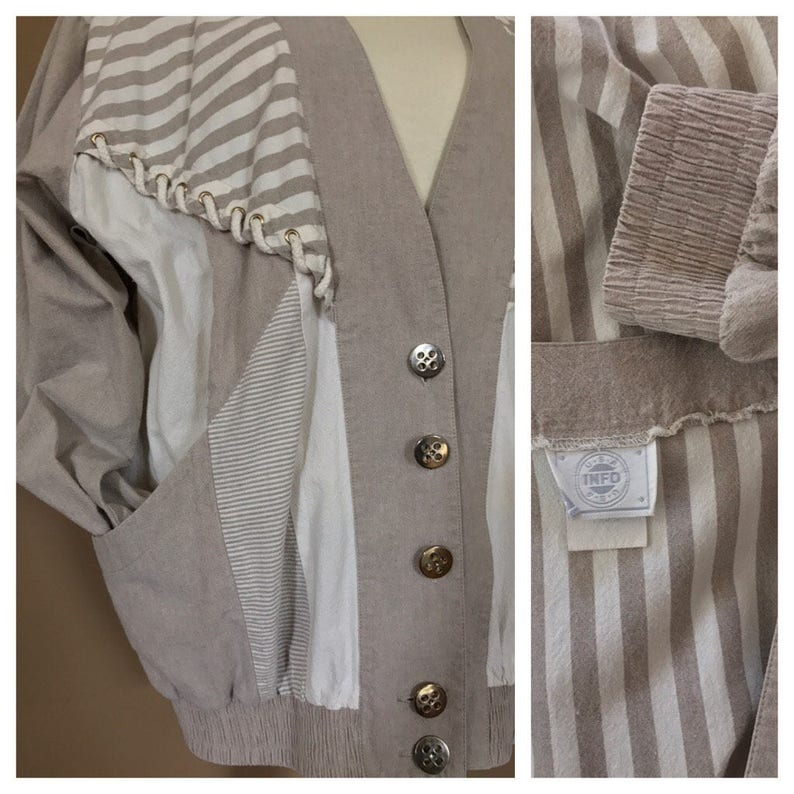 May include: A beige, striped, button-up jacket with a white and beige striped panel on the left side. The jacket has a V-neck and a label that reads "INFO" on the inside.