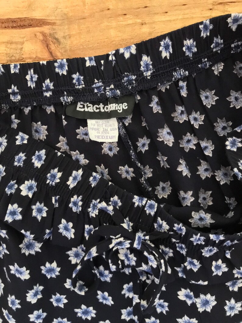Puede incluir: Pantal&oacute;n azul marino con estampado floral blanco y cintura con cord&oacute;n. El pantal&oacute;n tiene una etiqueta que dice "Elastounge" y "Medium".