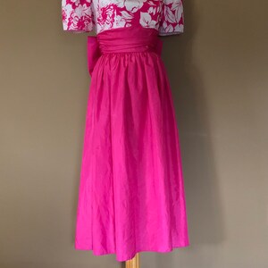 Puede incluir: Un vestido rosa con un corpi&ntilde;o de estampado floral blanco y una falda completa. El vestido tiene un lazo en la cintura y mangas cortas abullonadas.