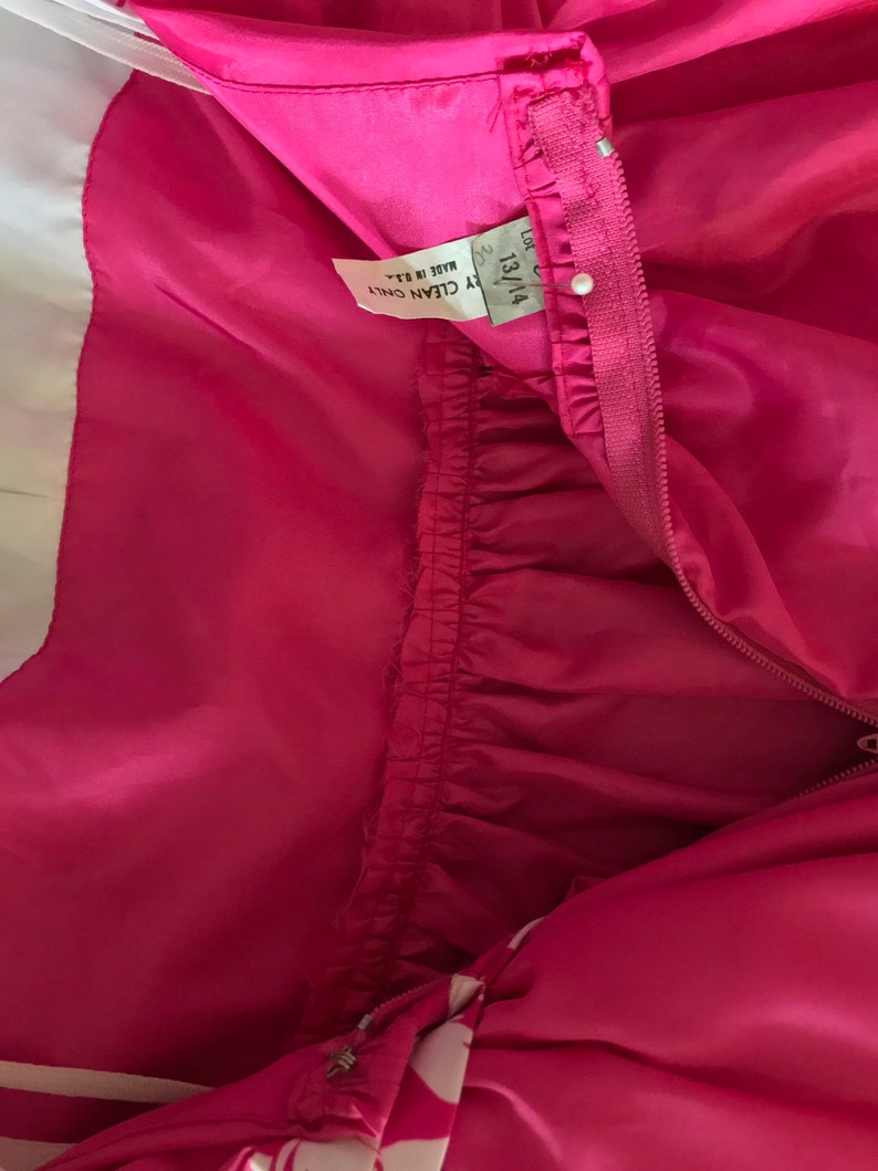 Puede incluir: Vestido rosa con estampado blanco y rosa. El vestido tiene una cremallera y una etiqueta que dice "13/14 Y CLEAN ONLY Made in B.R."