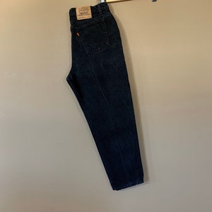 May include: Black denim jeans hanging on a wooden hanger. The jeans have a brown leather patch with the Levi's logo and the text "Levi's Strauss & Co. San Francisco, Calif. 94105" on the back.