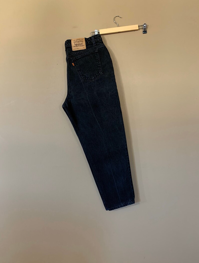 May include: Black denim jeans hanging on a wooden hanger. The jeans have a brown leather patch with the Levi's logo and the text "Levi's Strauss & Co. San Francisco, Calif. 94105" on the back.