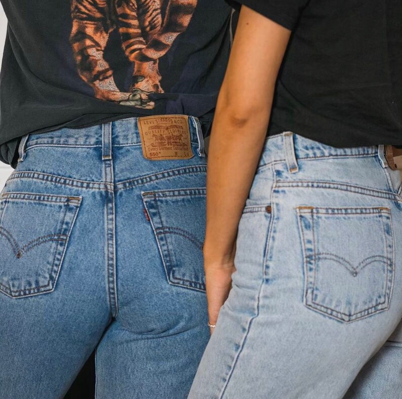May include: Two pairs of blue denim jeans. One pair is a medium wash with a red Levi's tag on the back pocket. The other pair is a lighter wash. Both pairs have the Levi's logo on the back pockets.