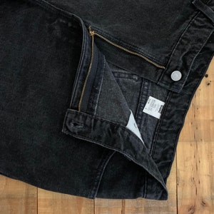 May include: Black denim jeans with a zipper fly and a Levi's label. The jeans are folded in half and the inside of the waistband is visible.