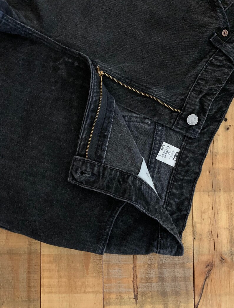 May include: Black denim jeans with a zipper fly and a Levi's label. The jeans are folded in half and the inside of the waistband is visible.