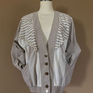 May include: A beige and white striped jacket with a V-neck and button closure. The jacket has a unique design with different panels of fabric.