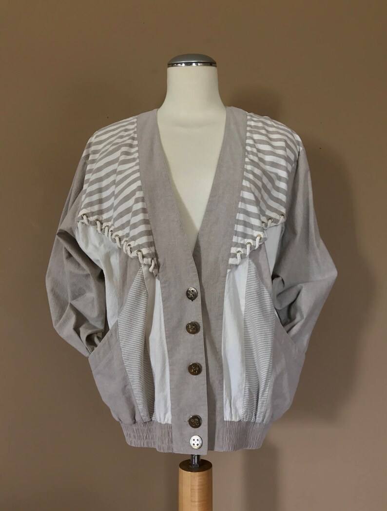 May include: A beige and white striped jacket with a V-neck and button closure. The jacket has a unique design with different panels of fabric.