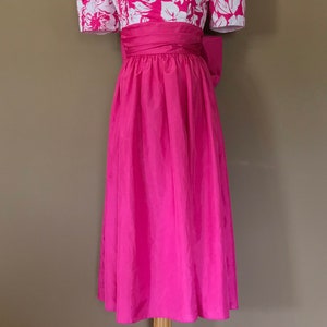 Puede incluir: Un vestido rosa con un corpi&ntilde;o de estampado floral blanco y una falda rosa lisa. El vestido tiene mangas abullonadas y un lazo en la cintura.