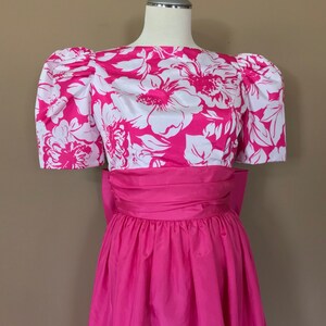 Puede incluir: Un vestido de estampado floral rosa y blanco con manga abullonada y una cinta a juego. El vestido tiene una falda completa y est&aacute; hecho de una tela ligera.