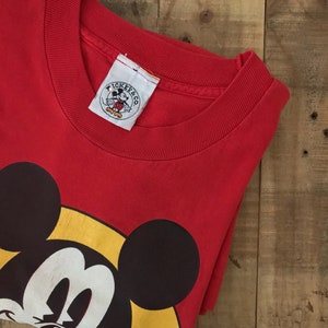May include: Red t-shirt with a large Mickey Mouse graphic on the front. The shirt has a crew neck and a tag that says "Mickey & Co."