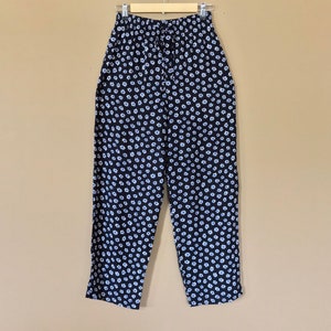 Puede incluir: Pantal&oacute;n negro con estampado floral blanco. El pantal&oacute;n tiene una cintura el&aacute;stica y un cord&oacute;n.