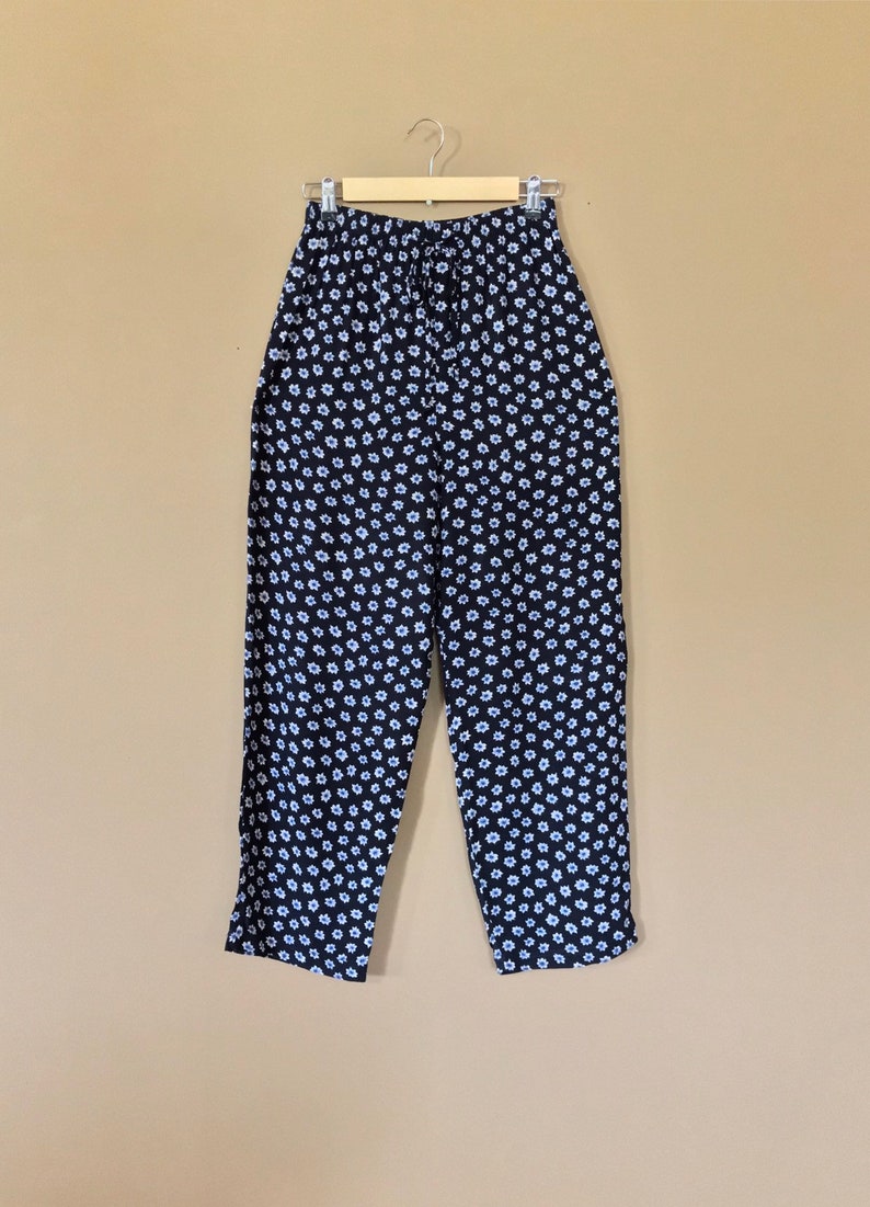Puede incluir: Pantal&oacute;n negro con estampado floral blanco. El pantal&oacute;n tiene una cintura el&aacute;stica y un cord&oacute;n.