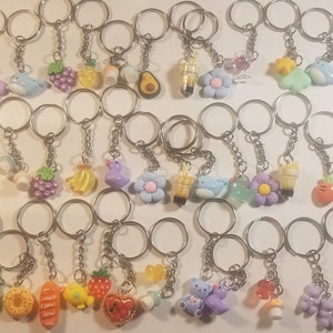 May include: A collection of 30 colourful keychains featuring various cute designs, including fruit, food, animals, and flowers. The keychains are made of plastic and have silver metal rings.