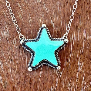 May include: A silver necklace featuring a turquoise star pendant. The star has a textured border and is suspended from a delicate chain. The pendant's bright turquoise color contrasts with the silver chain, creating a striking visual.