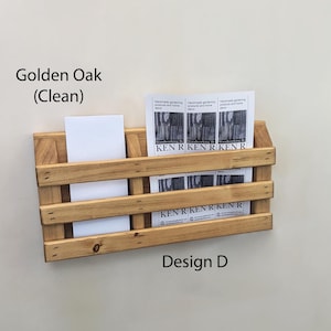 May include: A wooden wall-mounted organizer in Golden Oak, Design D, with a clean finish. It features multiple horizontal slats and holds white cards and printed papers. The text "KEN R KEN R KEN R" is visible on the papers.