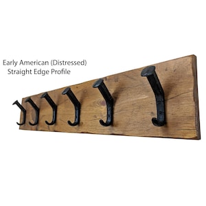 May include: A rustic wooden coat rack with six black metal hooks. The wood has a distressed finish and a straight edge profile. The text "Early American (Distressed) Straight Edge Profile" is visible.