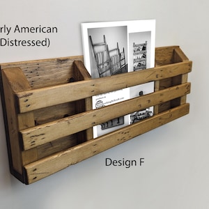 May include: A wall-mounted wooden rack with a distressed Early American finish, featuring three horizontal slats and two open compartments. A white paper insert with black and white images and the text Early American (Distressed) Design F is visible.