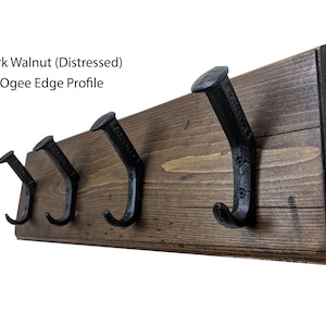 May include: A dark walnut wood coat rack with a distressed finish and an ogee edge profile. The rack has four black metal hooks.