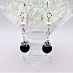 May include: A pair of silver dangle earrings with black onyx and white pearl beads. The earrings have a silver filigree design on the onyx beads.