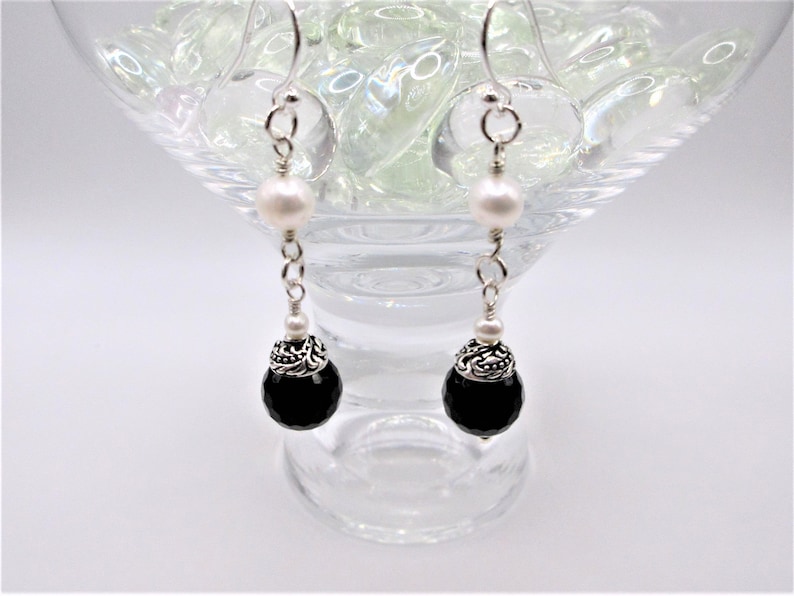 May include: A pair of silver dangle earrings with black onyx and white pearl beads. The earrings have a silver filigree design on the onyx beads.