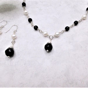 May include: A black and white pearl necklace with a black onyx pendant and matching black onyx earrings. The necklace and earrings are made with silver chain and beads.
