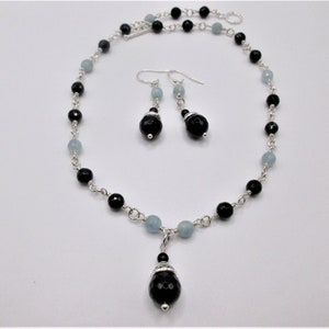 May include: A silver necklace and earrings set with black and light blue beads. The necklace has a pendant with a large black bead.