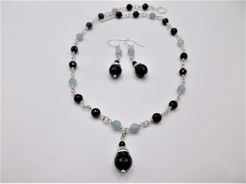 May include: A silver necklace and earrings set with black and light blue beads. The necklace has a pendant with a large black bead.