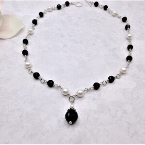 May include: A black and white beaded necklace with a silver chain and a black gemstone pendant.