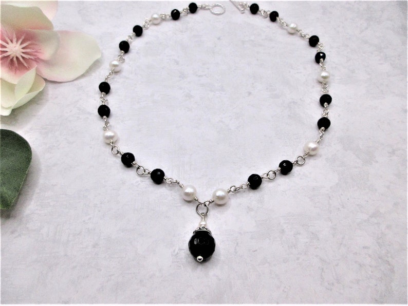 May include: A black and white beaded necklace with a silver chain and a black gemstone pendant.