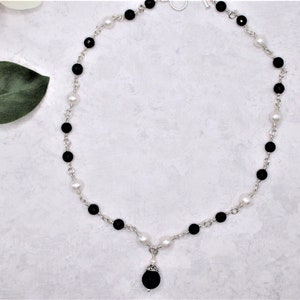 May include: A silver chain necklace with alternating black and white beads. The necklace has a black bead pendant.