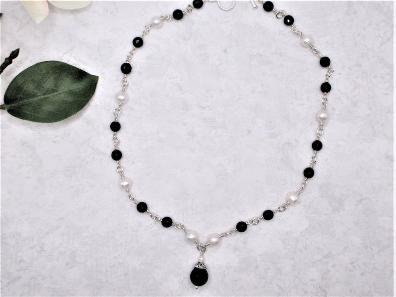 May include: A silver chain necklace with alternating black and white beads. The necklace has a black bead pendant.