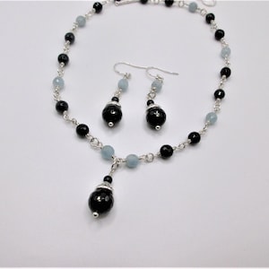 May include: A silver necklace and earrings set with black and light blue beads. The necklace has a pendant with a larger black bead.