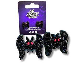 May include: A pair of black glitter bat earrings with pink eyes. The earrings are hypoallergenic and are sold by The Strange Charm.