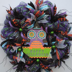 May include: A Halloween wreath with black, purple, orange, and green mesh and ribbons. A purple owl with orange and green accents and a sign that says "Happy Halloween" are in the center of the wreath.