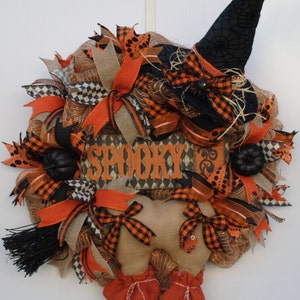 May include: A Halloween wreath with a witch figure, a black witch hat, orange and black ribbon, and a sign that says "Spooky".