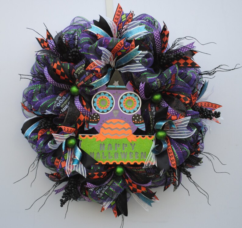 May include: A Halloween wreath with black, purple, orange, and green mesh and ribbons. A purple owl with orange and green accents and a sign that says "Happy Halloween" are in the center of the wreath.