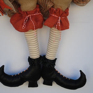 May include: A pair of black witch boots with orange accents and a striped fabric leg. The boots have pointed toes and a curved heel.