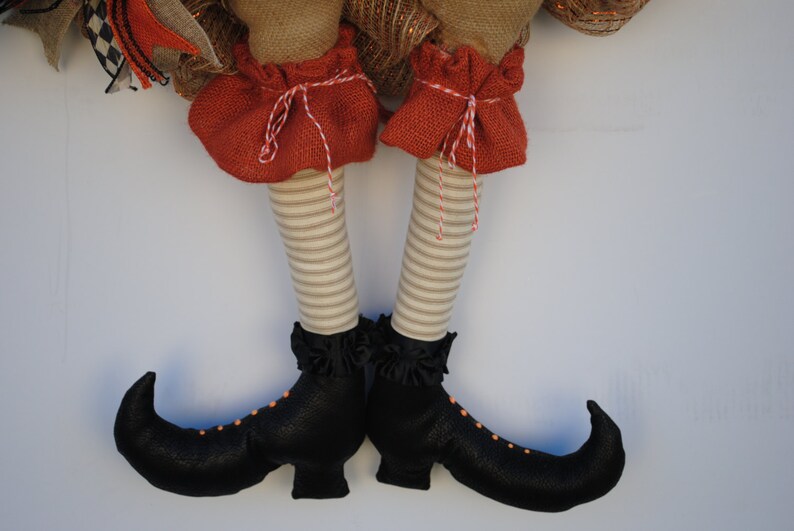 May include: A pair of black witch boots with orange accents and a striped fabric leg. The boots have pointed toes and a curved heel.