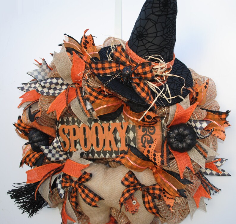 May include: A Halloween wreath with a black witch hat, orange and black checkered ribbon, burlap, and a wooden sign that says "Spooky".