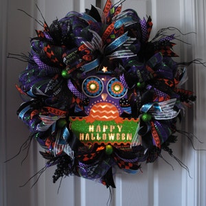 May include: A Halloween wreath with black, purple, green, and orange mesh and ribbons. A light-up owl with the words "Happy Halloween" is in the center.