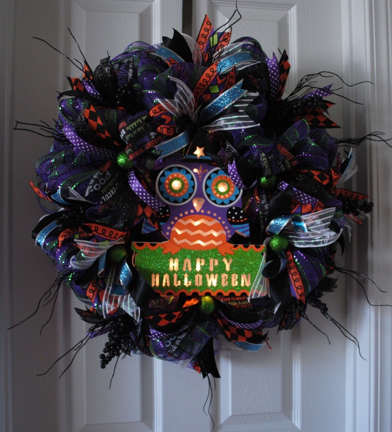 May include: A Halloween wreath with black, purple, green, and orange mesh and ribbons. A light-up owl with the words "Happy Halloween" is in the center.