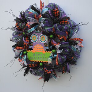 May include: A Halloween wreath with black, purple, orange, and green mesh, ribbons, and a wooden owl cutout with the words "Happy Halloween".