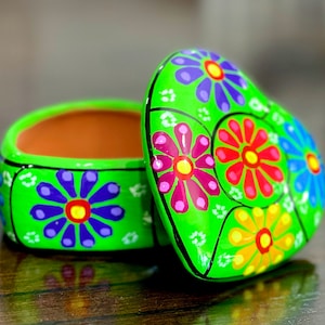 Pode incluir: Uma caixa de coração verde com tampa. A caixa é decorada com flores coloridas pintadas em rosa, vermelho, amarelo, azul e verde.