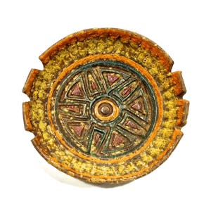 Puede incluir: Un plato redondo de cerámica con un diseño geométrico en tonos de verde, naranja y amarillo. El plato tiene una superficie texturizada y un borde elevado.